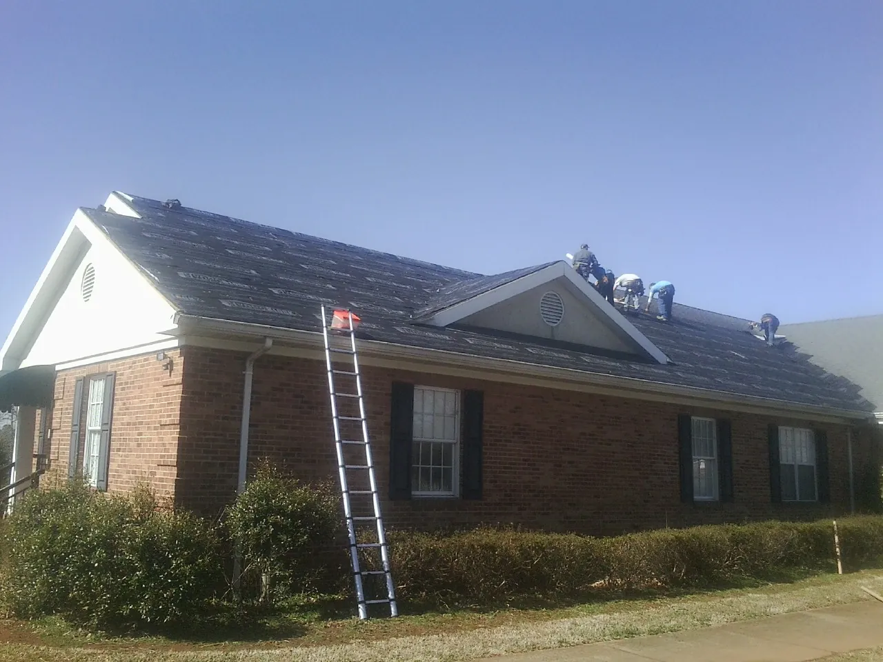 Crew tearing shingles off a brick ranch roof with a ladder set — Metal Roof Repair work by our crew in Ottertail