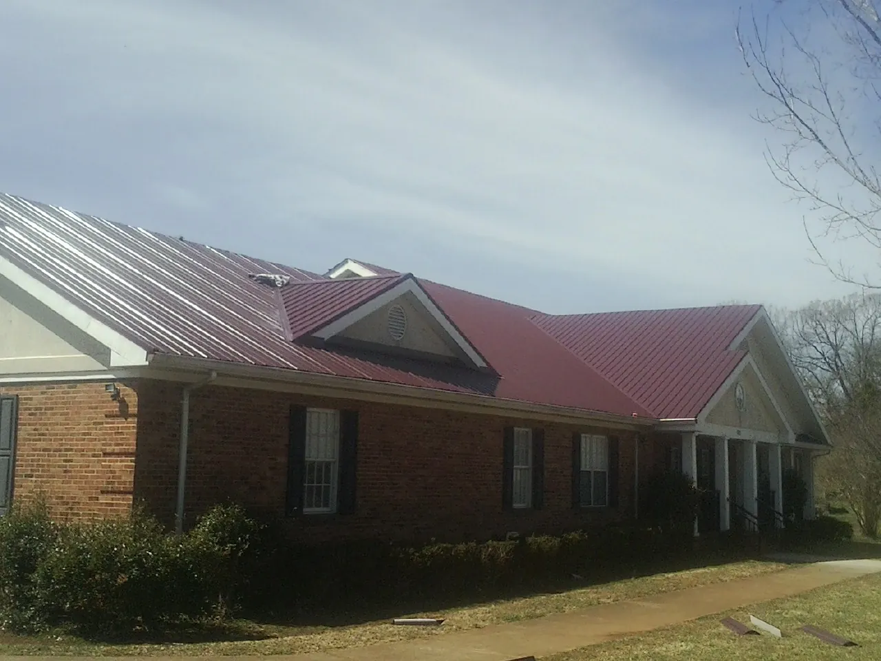 Red metal roof with gabled entries on a long brick building, from a Hail Damage Roof Repair job in Ottertail