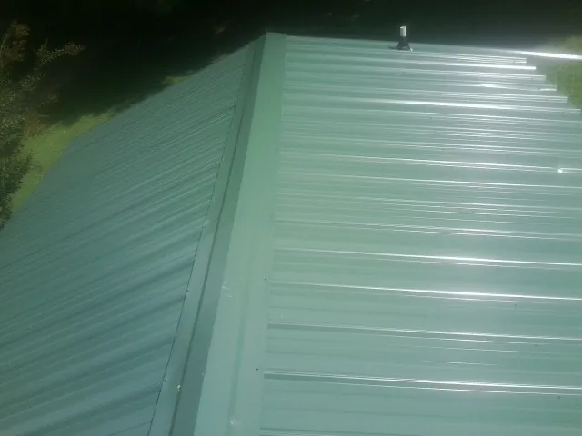 New green metal panels meeting at the ridge of a roof — Flat Roof Repair work by our crew in Ottertail