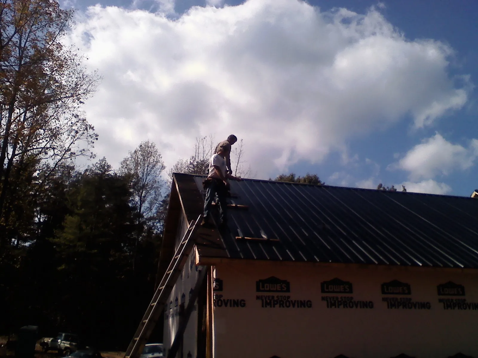 Roofer fastening dark metal panels high against a cloudy sky, from a Roof Inspection job in Ottertail